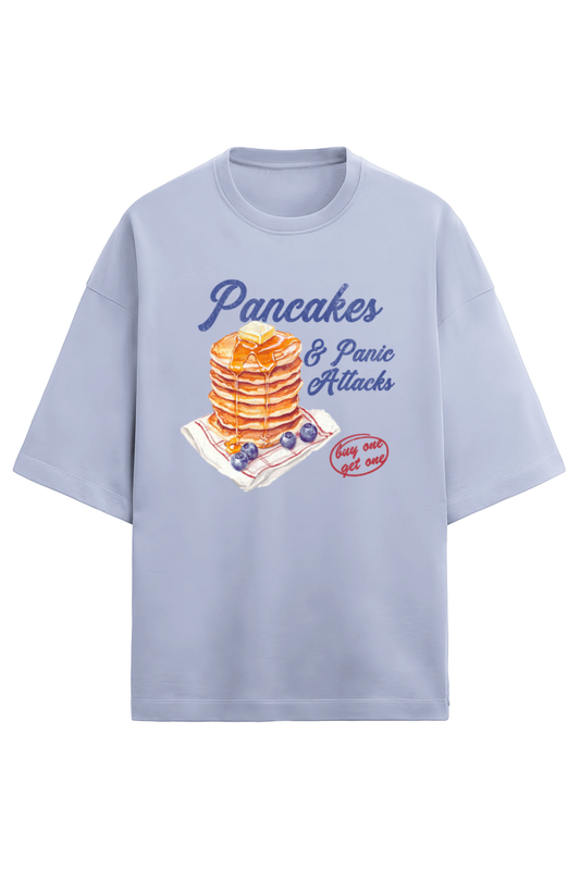 A lavender oversized French Terry T-shirt made of 280 GSM cotton featuring the bold and quirky text "Pancake & Panic Attack" printed on the front. The T-shirt is styled for a casual, unisex look with a soft and heavyweight feel.