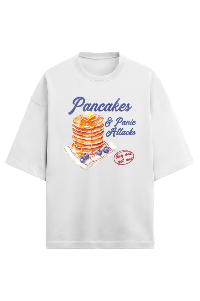A white oversized French Terry T-shirt made of 280 GSM cotton featuring the bold and quirky text "Pancake & Panic Attack" printed on the front. The T-shirt is styled for a casual, unisex look with a soft and heavyweight feel.