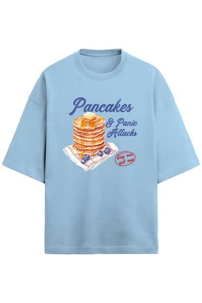A baby blue oversized French Terry T-shirt made of 280 GSM cotton featuring the bold and quirky text "Pancake & Panic Attack" printed on the front. The T-shirt is styled for a casual, unisex look with a soft and heavyweight feel.