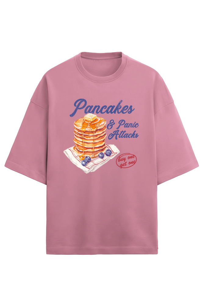 A pink oversized French Terry T-shirt made of 280 GSM cotton featuring the bold and quirky text "Pancake & Panic Attack" printed on the front. The T-shirt is styled for a casual, unisex look with a soft and heavyweight feel.