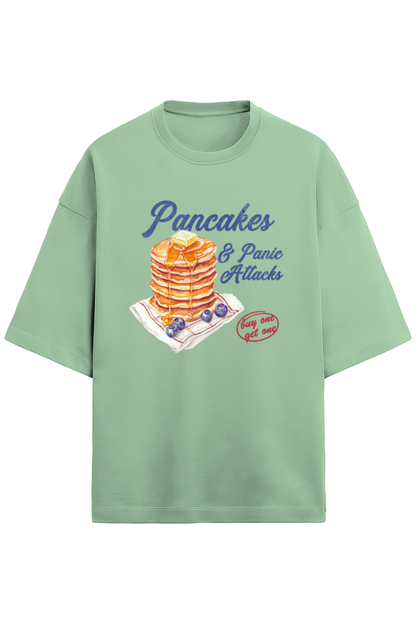 A jade, green oversized French Terry T-shirt made of 280 GSM cotton featuring the bold and quirky text "Pancake & Panic Attack" printed on the front. The T-shirt is styled for a casual, unisex look with a soft and heavyweight feel.