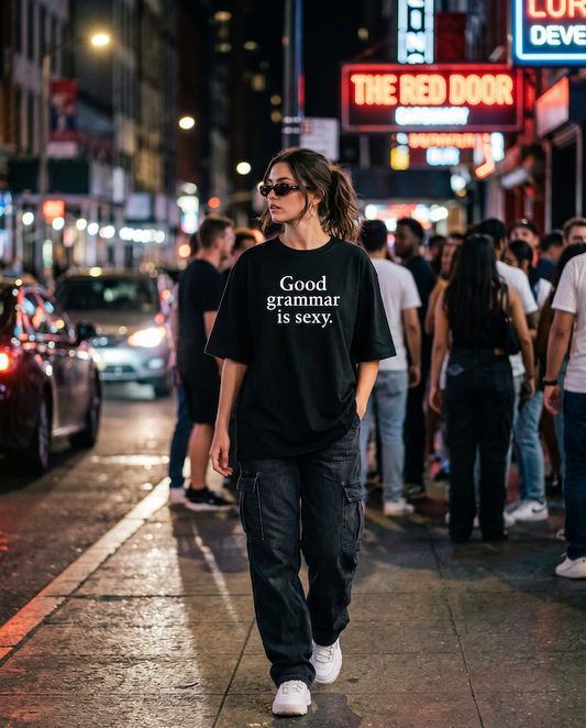 Person wearing a black Good Grammar Is Sexy Oversized T-Shirt - Minimalist Graphic Tee on a city street at night.