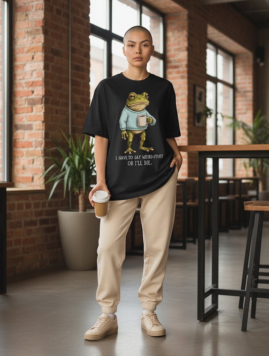Frolic Saga black oversized t-shirt with a graphic of a frog wearing a blue sweater and holding a coffee cup, text reads "I HAVE TO SAY WEIRD STUFF OR I'LL DIE."