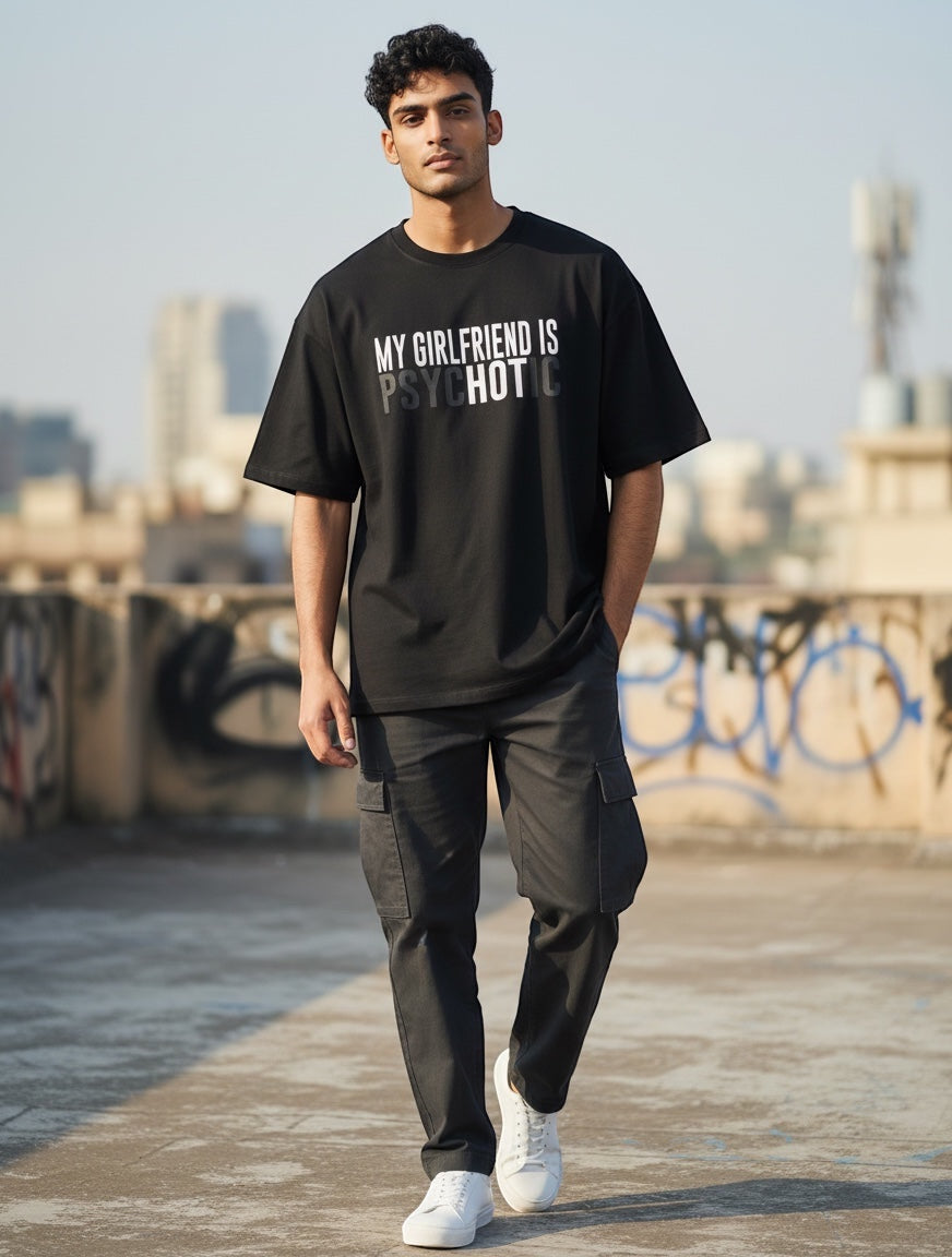 Frolic Saga black 100% cotton oversized tee with "My Girlfriend Is Psychotic" graphic print, worn by a male model.