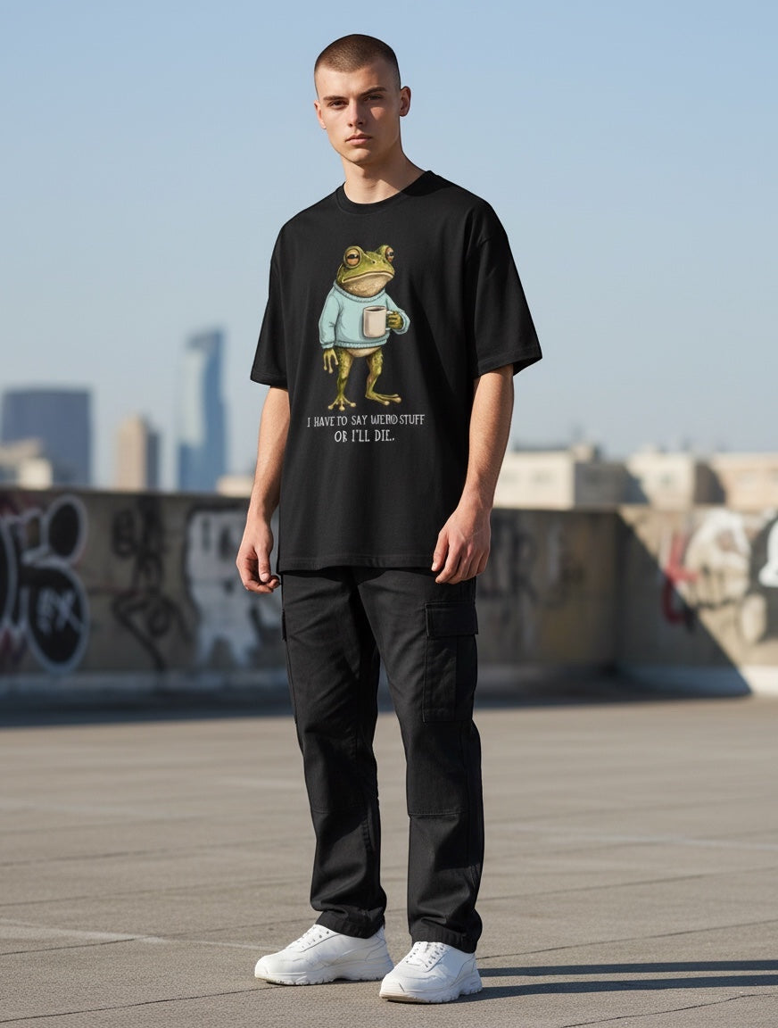 Frolic Saga black oversized cotton t-shirt with a graphic of a frog wearing a sweater and holding a mug, text reads "I HAVE TO SAY WEIRD STUFF OR I'LL DIE."