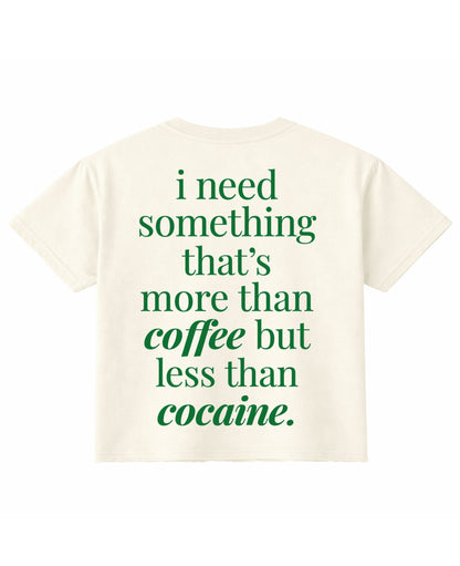 Frolic Saga cream cropped t-shirt with green text on the back reading I need something that is more than coffee