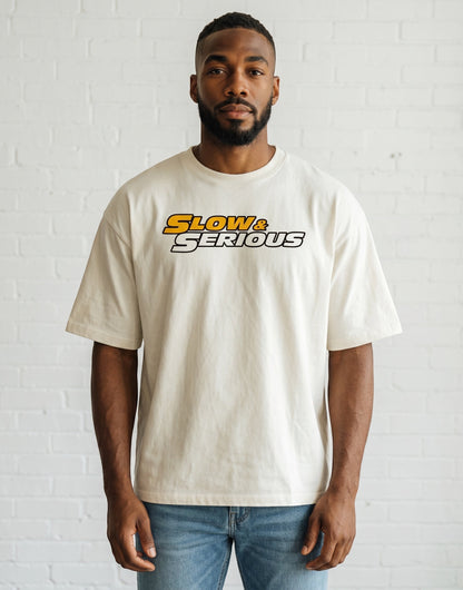 Frolic Saga unisex oversized cream cotton t-shirt with Slow & Serious graphic print worn by a man.