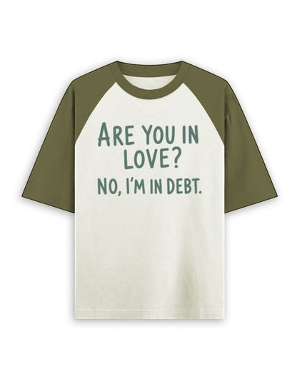 Cream and olive green oversized raglan t-shirt featuring the dark green text ARE YOU IN LOVE? NO, I'M IN DEBT.
