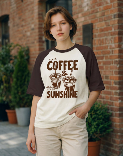 Frolic Saga oversized raglan t-shirt with iced coffee graphic, cream and brown cotton, worn by a woman outdoors.