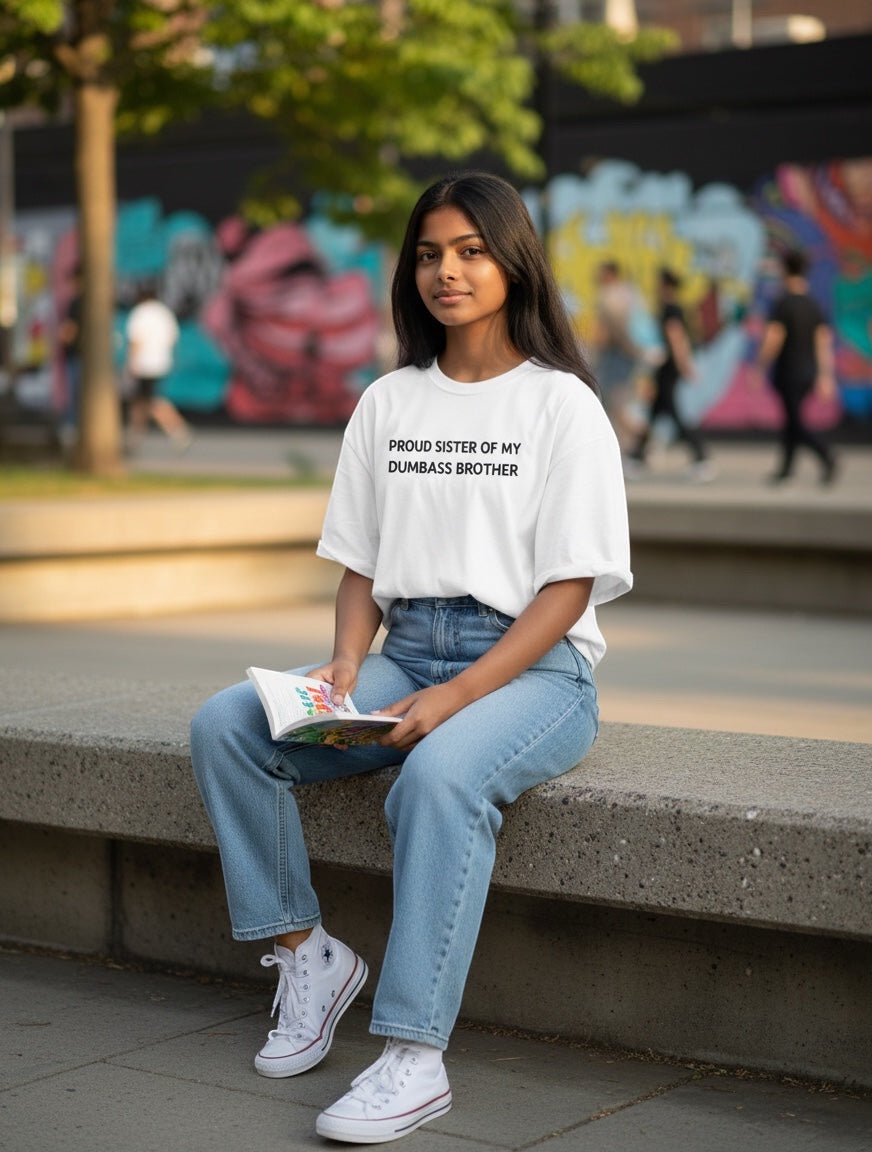 Frolic Saga white oversized t-shirt with black text reading "Proud Sister Of My Dumbass Brother", worn by a young woman with light wash jeans.