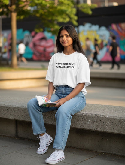 Frolic Saga white oversized t-shirt with black text reading "Proud Sister Of My Dumbass Brother", worn by a young woman with light wash jeans.