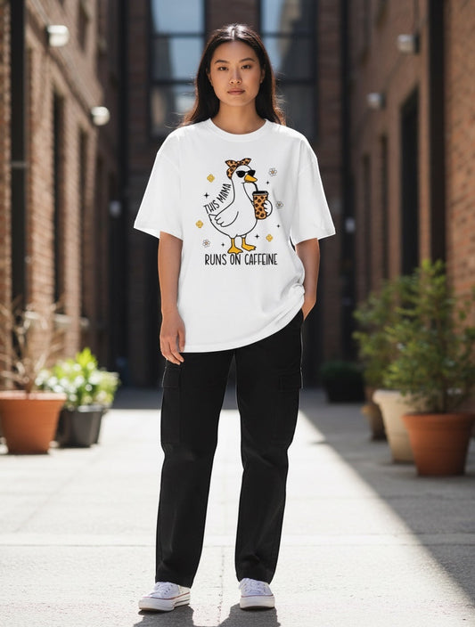 Frolic Saga white 100% cotton oversized t-shirt with a graphic of a duck wearing sunglasses and a bandana, holding a coffee cup. Text reads "This Mama Runs On Caffeine".